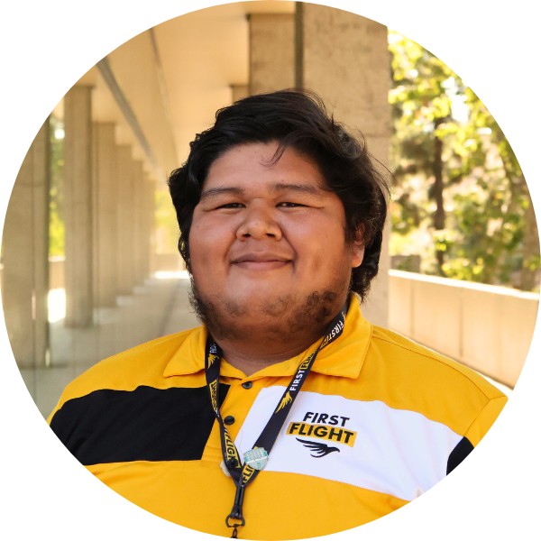 A man with a yellow and black polo that reads "First Flight" staring into the camera.