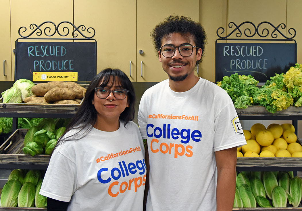 Two students wearing matching College Corps t-shirts, standing inside a food pantry.