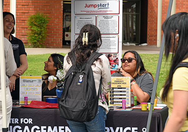 A student wearing a backpack speaks with a staff person at an event table.