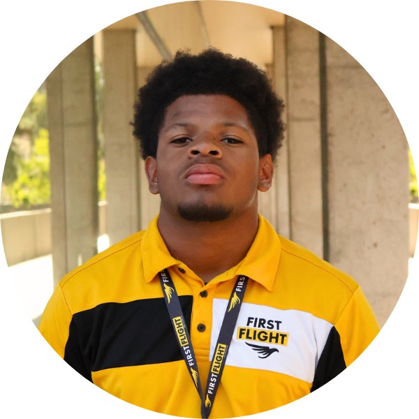 A man with a yellow and black polo that reads "First Flight" staring into the camera.