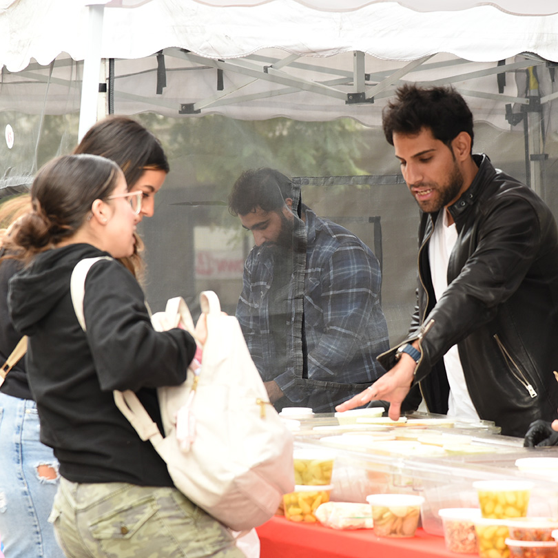 A student with a tote bag over her shoulder speaks with a food vendor.