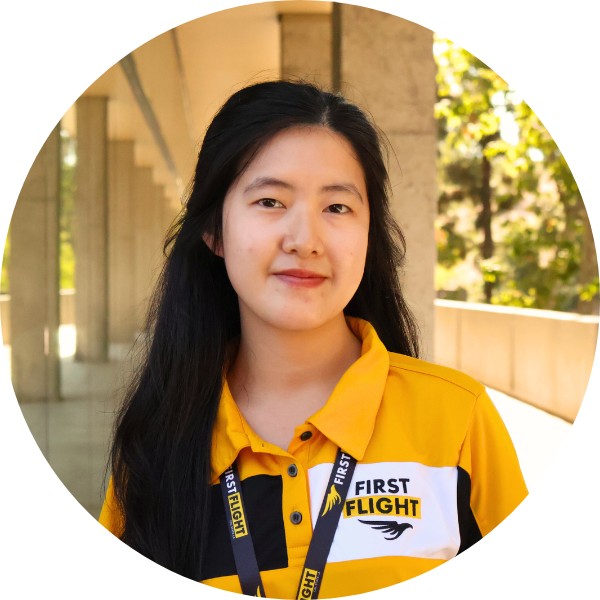 A woman with a yellow and black polo that reads "First Flight" smiling toward the camera.