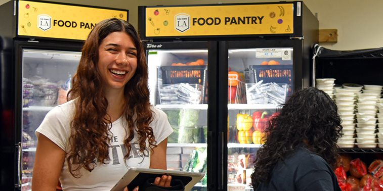 Person smiling with a tablet in front of refrigerators with Cal State LA branding.
