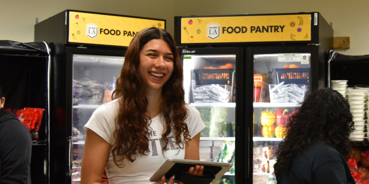 A person holding a tablet in front of a refrigerator at the food pantry.