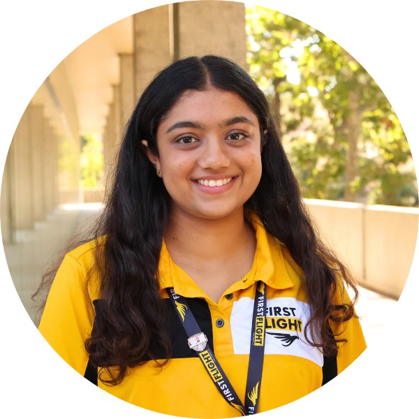 A woman with a yellow and black polo that reads "First Flight" smiling toward the camera.