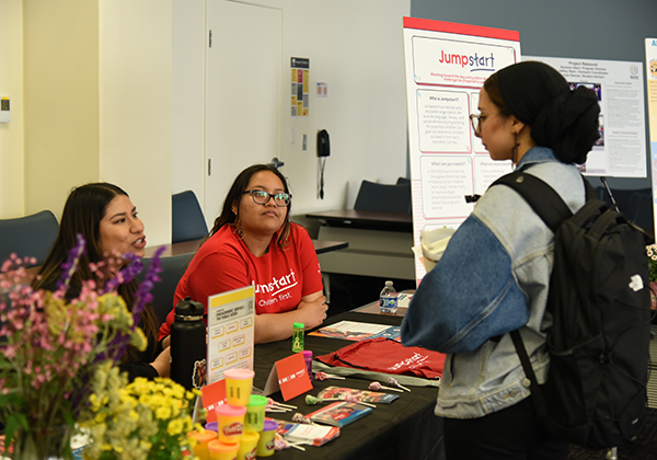 A student wearing a backpack speaks with a staff person at an event table.