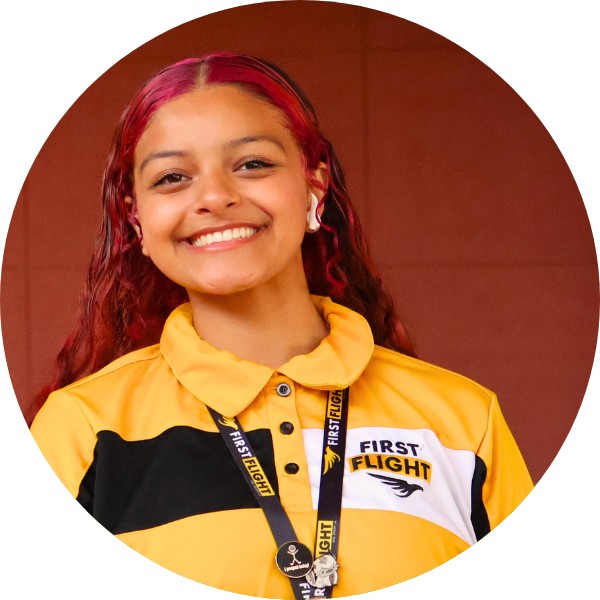 A woman with a yellow and black polo that reads "First Flight" smiling toward the camera.