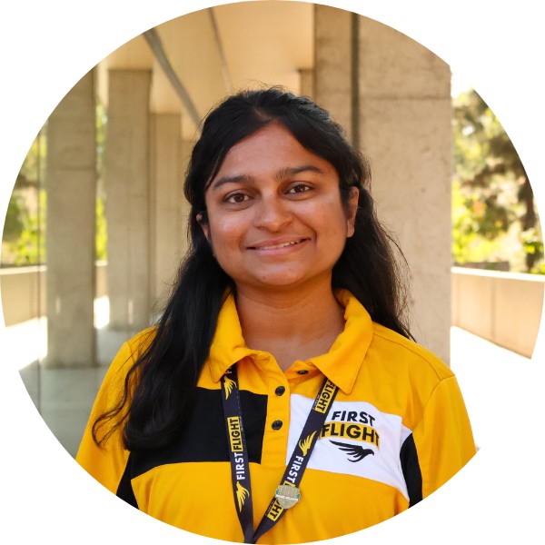 A woman with a yellow and black polo that reads "First Flight" smiling toward the camera.