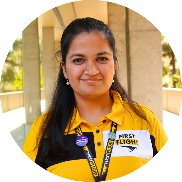 A woman with a yellow and black polo that reads "First Flight" smiling toward the camera.
