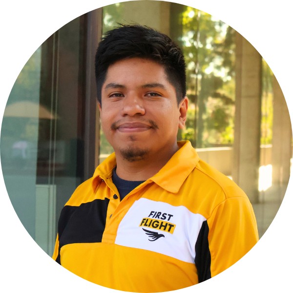 A man with a yellow and black polo that reads "First Flight" staring into the camera.