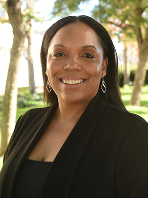 A person with long hair and earrings smiling.