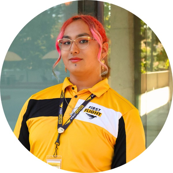 A person with pink reddish hair and a yellow and black polo smiling toward the camera.