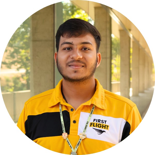 A man with a yellow and black polo that reads "First Flight" staring into the camera.
