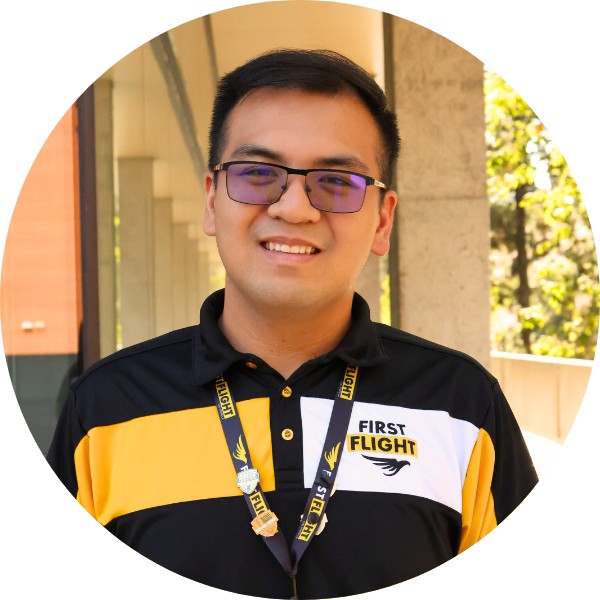 A man with black hair and a black polo smiling at the camera.