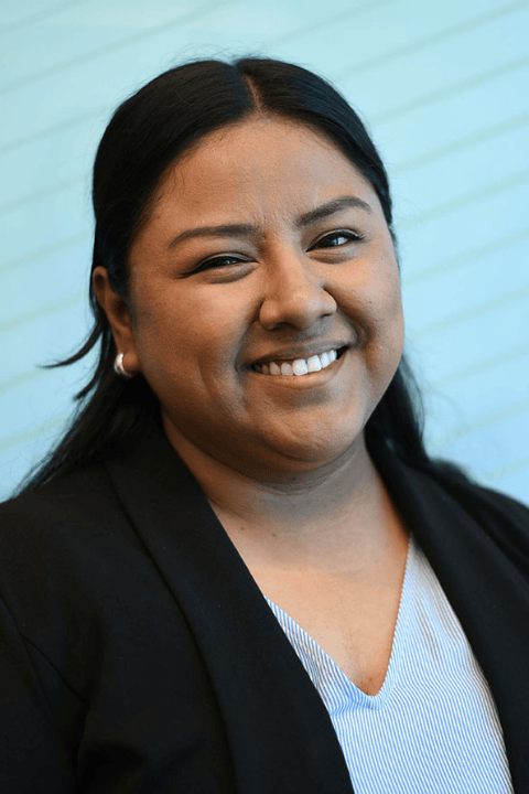 A person with long, dark hair pulled back smiling.