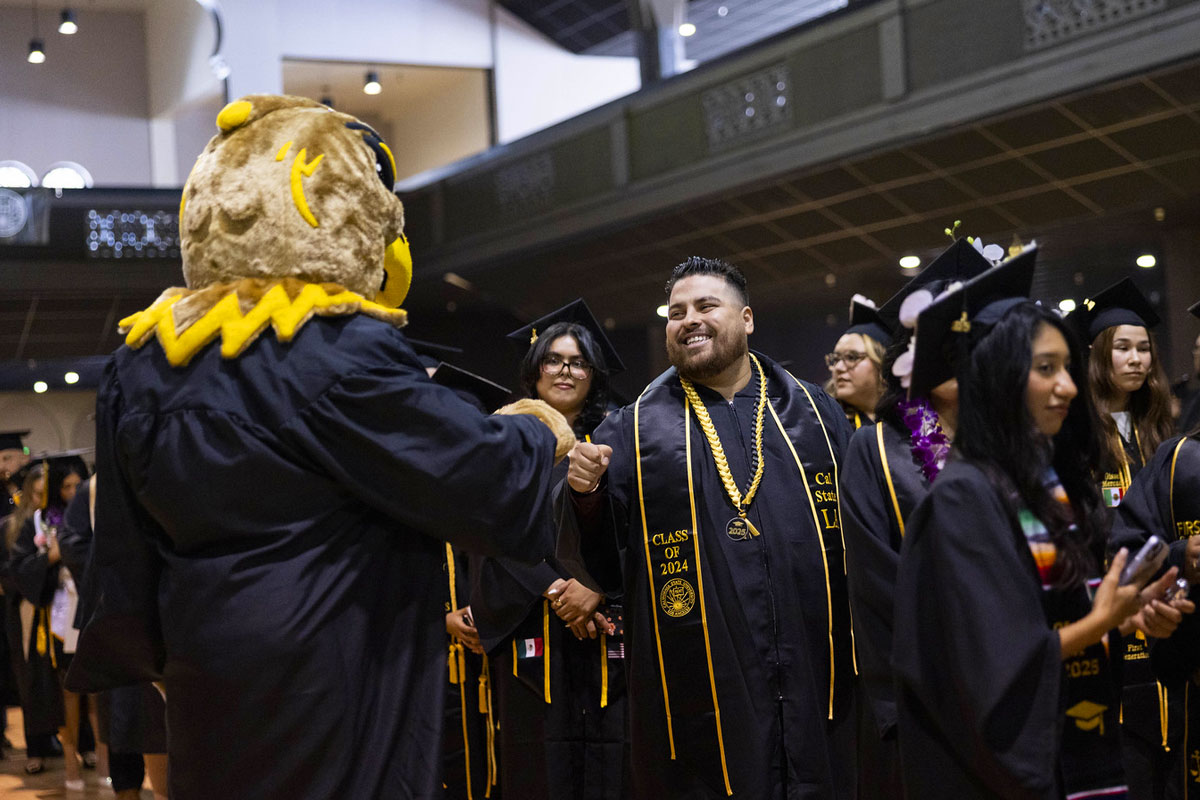 A mascot and a graduate bump fists in celebration.