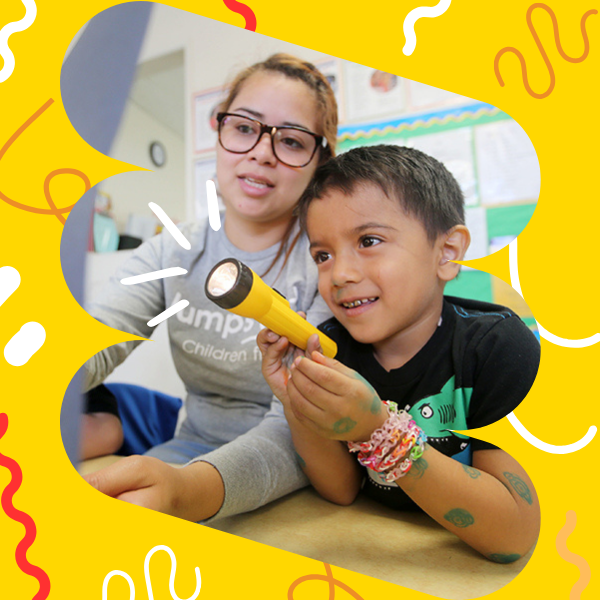 Child sitting next to teacher holding up a flashlight