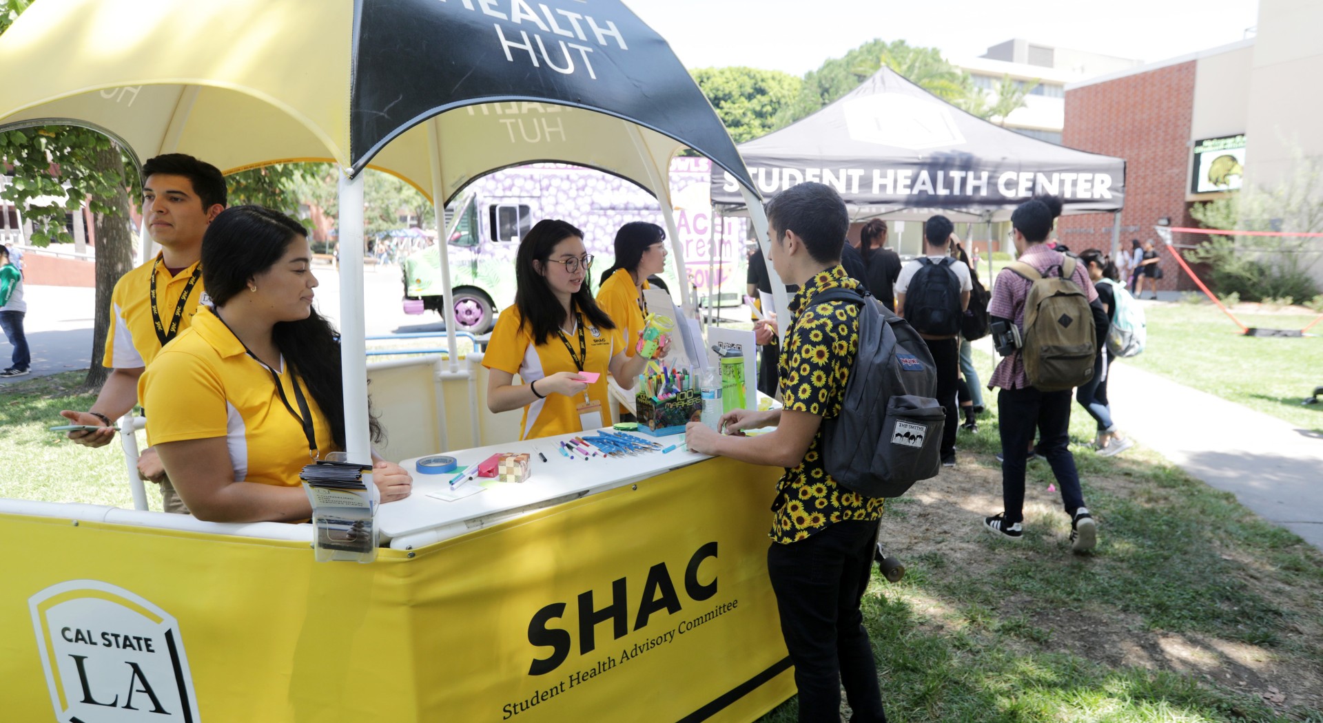 Three peer health educators staffing a Health Hut and educating a student.