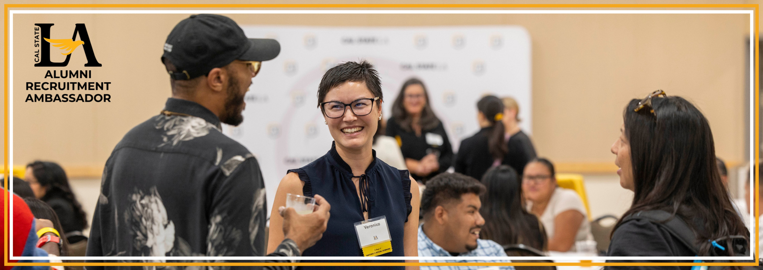 A woman smiling and laughing while talking to two other alumni
