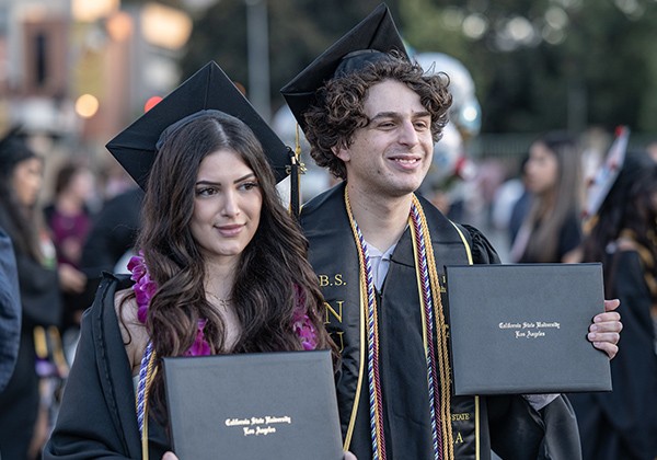 Two Students at Commencement holding Diplomas