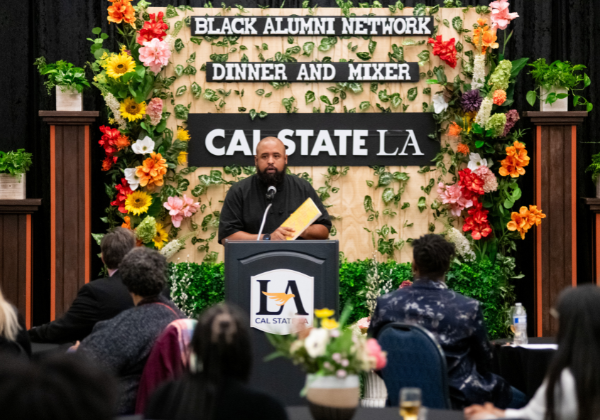 Man speaking at podium in front of sign that says Cal State LA Black Alumni Mixer and Dinner