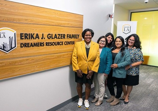 A group of women stand together smiling in a hallway next to a wall sign that reads “Erika J. Glazer Family Dreamers Resource Center.” 