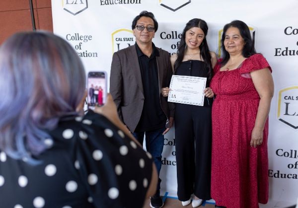Three people pose together in front of a backdrop.
