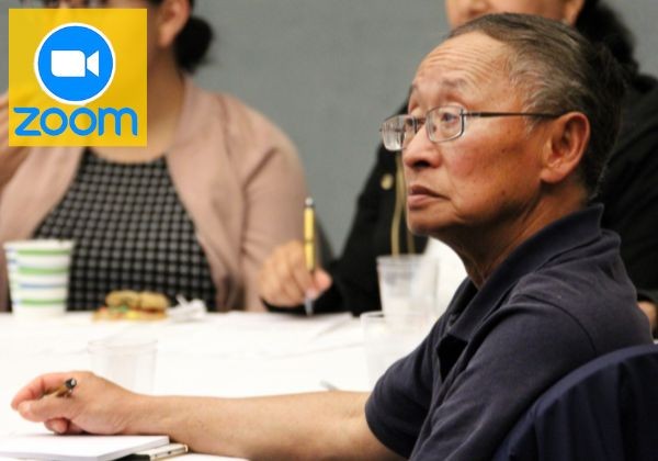 A man wearing glasses sits at a table. A Zoom logo in the corner suggests the event may be part of a virtual or hybrid session.