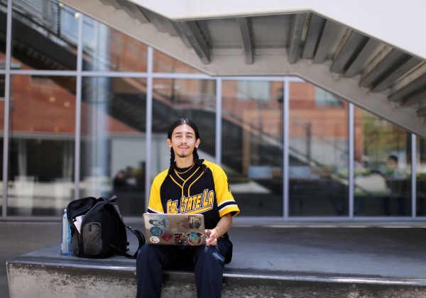 Student in Cal State LA clothing sits confidently outside while using a computer