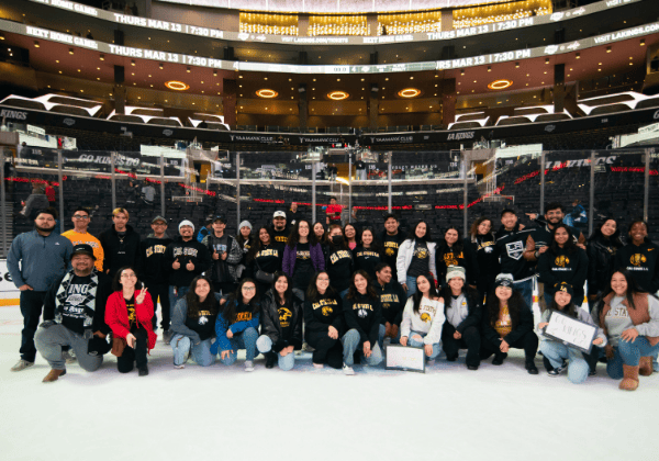 A group of about 50 people wearing Cal State LA shirts posing on the ice at Crypto.com Arena