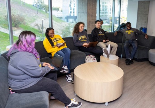 A small group of students sit in a lounge area , casually talking and relaxing.
