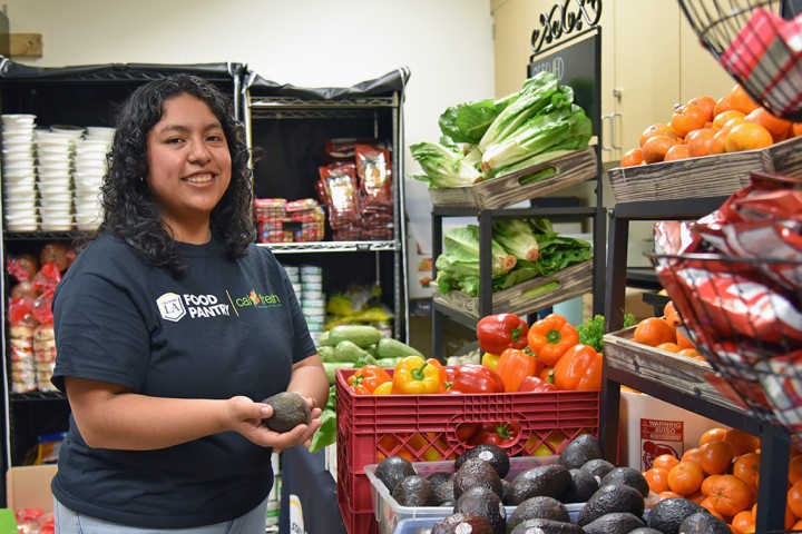 Person in a Cal State LA Food Pantry T-shirt standing in front of fresh produce bins.