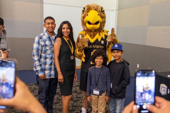 A family poses for a photo with a Cal State Los Angeles eagle mascot while someone takes the picture on a phone.