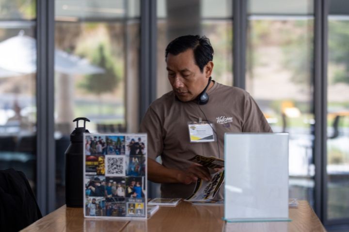 A man with a name tag looks at brochures at a table with a QR code display and water bottle