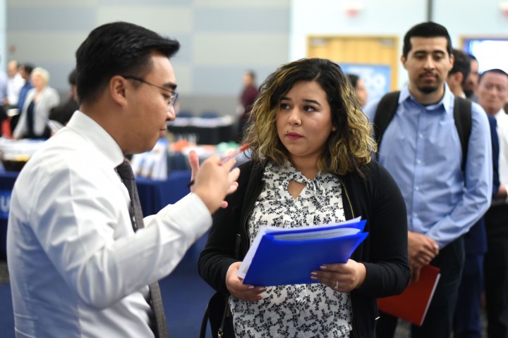 A student holds a portfolio and speaks with an employer at a career fair.