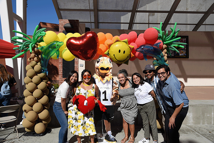 A group of people pose together outdoors under a colorful balloon arch