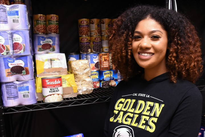 Smiling person in a Golden Eagles sweatshirt standing before shelves of nonperishable food.