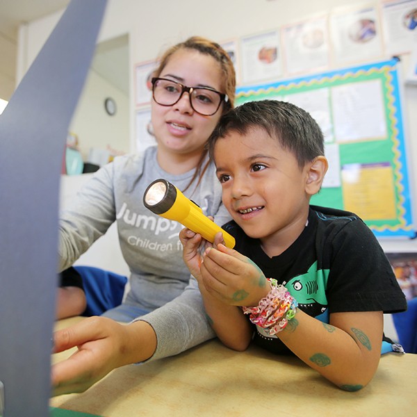 Child sitting next to teacher holding up a flashlight