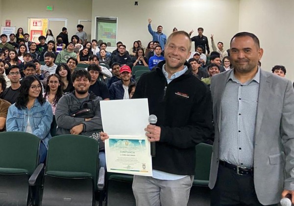 Dr Bachman stands in fromt of classroom of students with certificate smiling