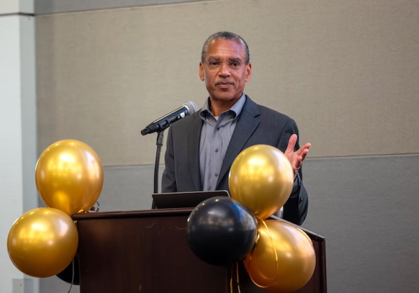 Dr. Stephen L. Mayo speaks at a podium during the Lloyd N. Ferguson Distinguished Lecture at Cal State LA, with gold and black balloons decorating the front.