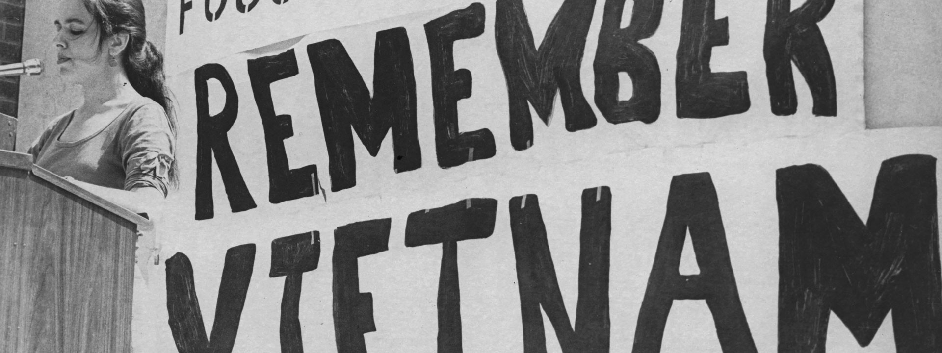A speaker giving a speech in front of a Remember Vietnam sign